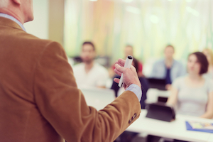 Man wearing a brown blazer gives a class to adult students