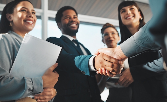 Two people shaking hands surrounded by three women smiling