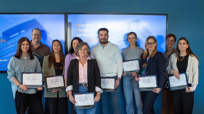 Photo of a diverse group of professionals holding certificates in front of a smart board