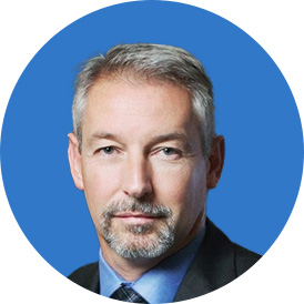Business man with gray hair wearing a black suit with a blue top smiling