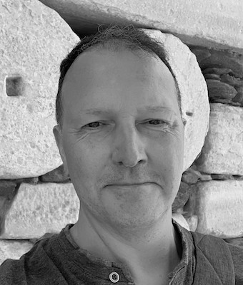 Black and white photo of a white man with stones in the backgound