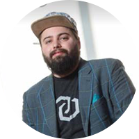 Business man wearing a checkered suit and a graphic shirt under it. He is wearing a snapback hair