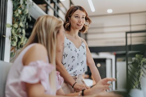 A photo of a young female professional standing up and leading a discussion, and wearing summer attire