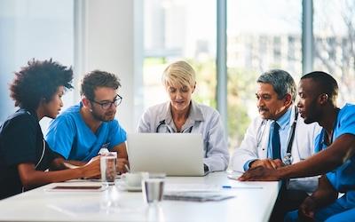 Diverse group of healthcare professionals during a meeting, sitting around the table and looking at a laptop