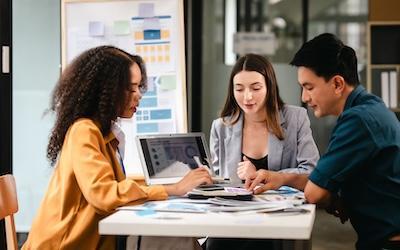 Group of three young employees talking around a computer having a meeting