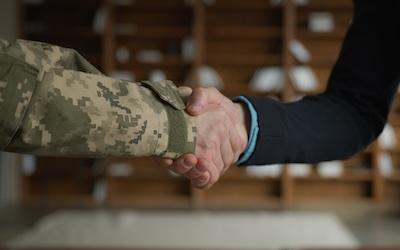 photo of two indivduals shaking hands. One is in a black suit, the other in military wear.