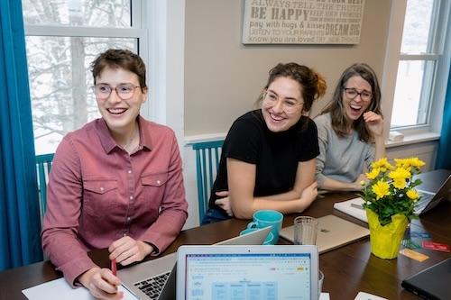 Photo of three woman laughing and sitting at a table that has flowers on it