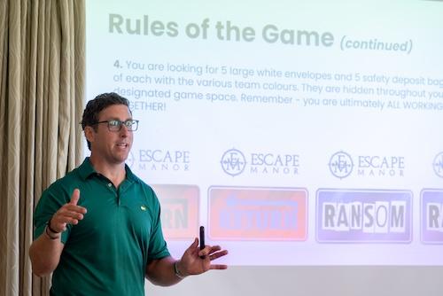 Photo of a business man wearing glass and a green polo shirt in front of a screen