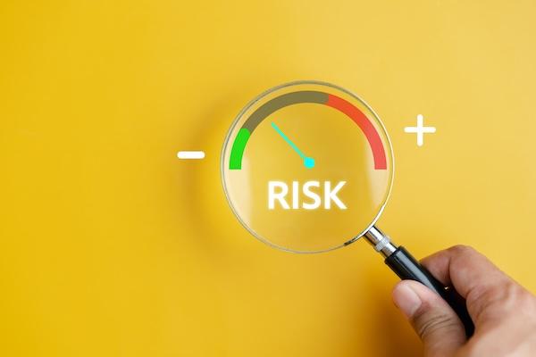 Image of an individal holding a magnifying glass to a graphic that says less risk on the left side, and more risk on the right side
