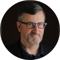 Photo of a white business man, wearing black glasses and a black button up