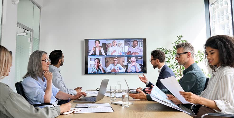 Diverse business people discuss in a meeting room and watching other people on the television screen.